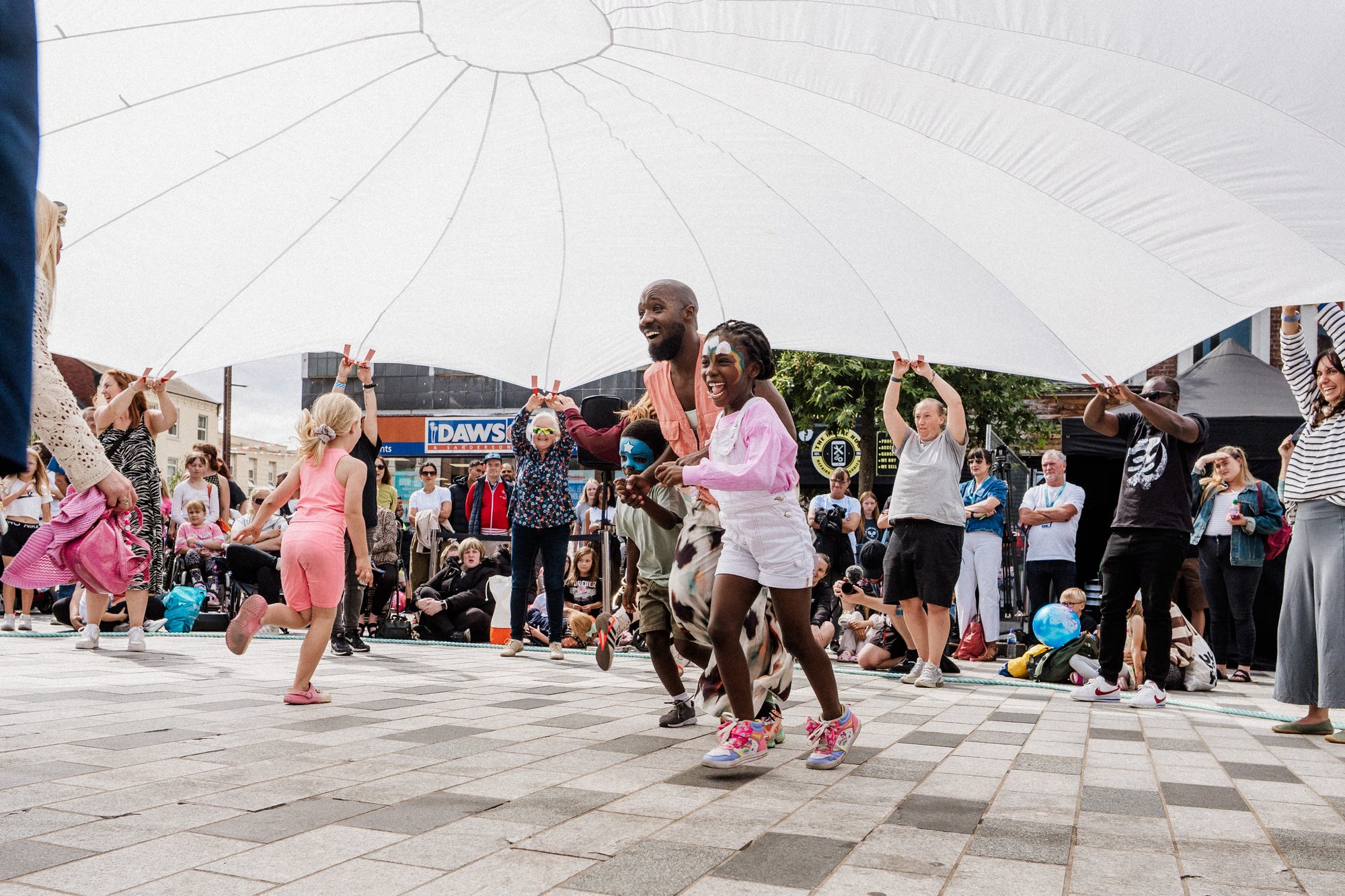 Two people running under a large parachute held by a group of people