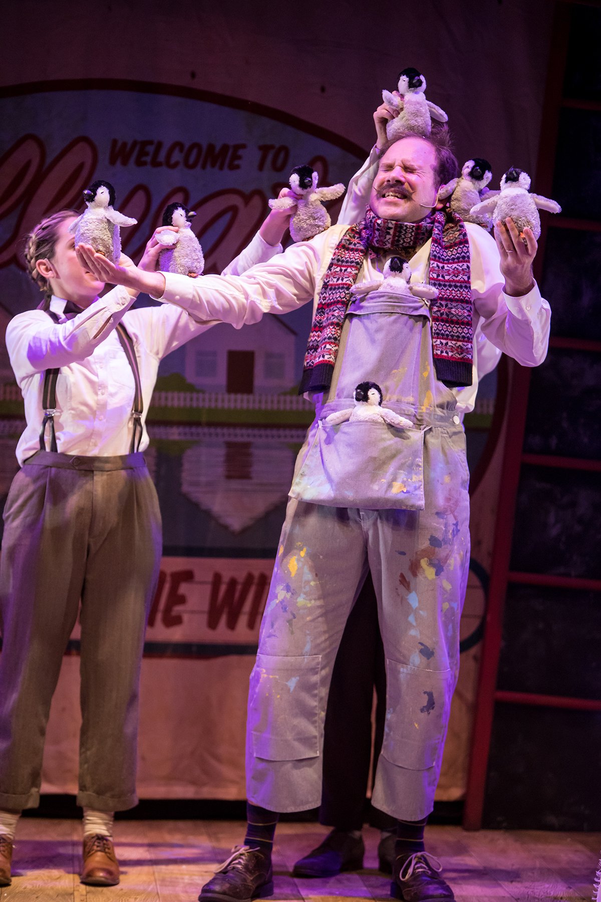 Man standing on stage with penguin puppets on him