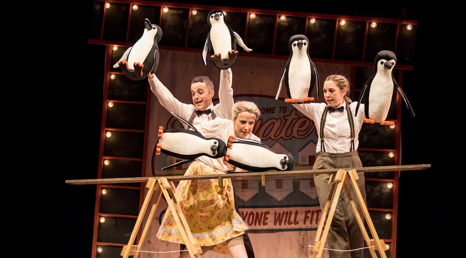 3 people on stage with penguin puppets performing acrobats