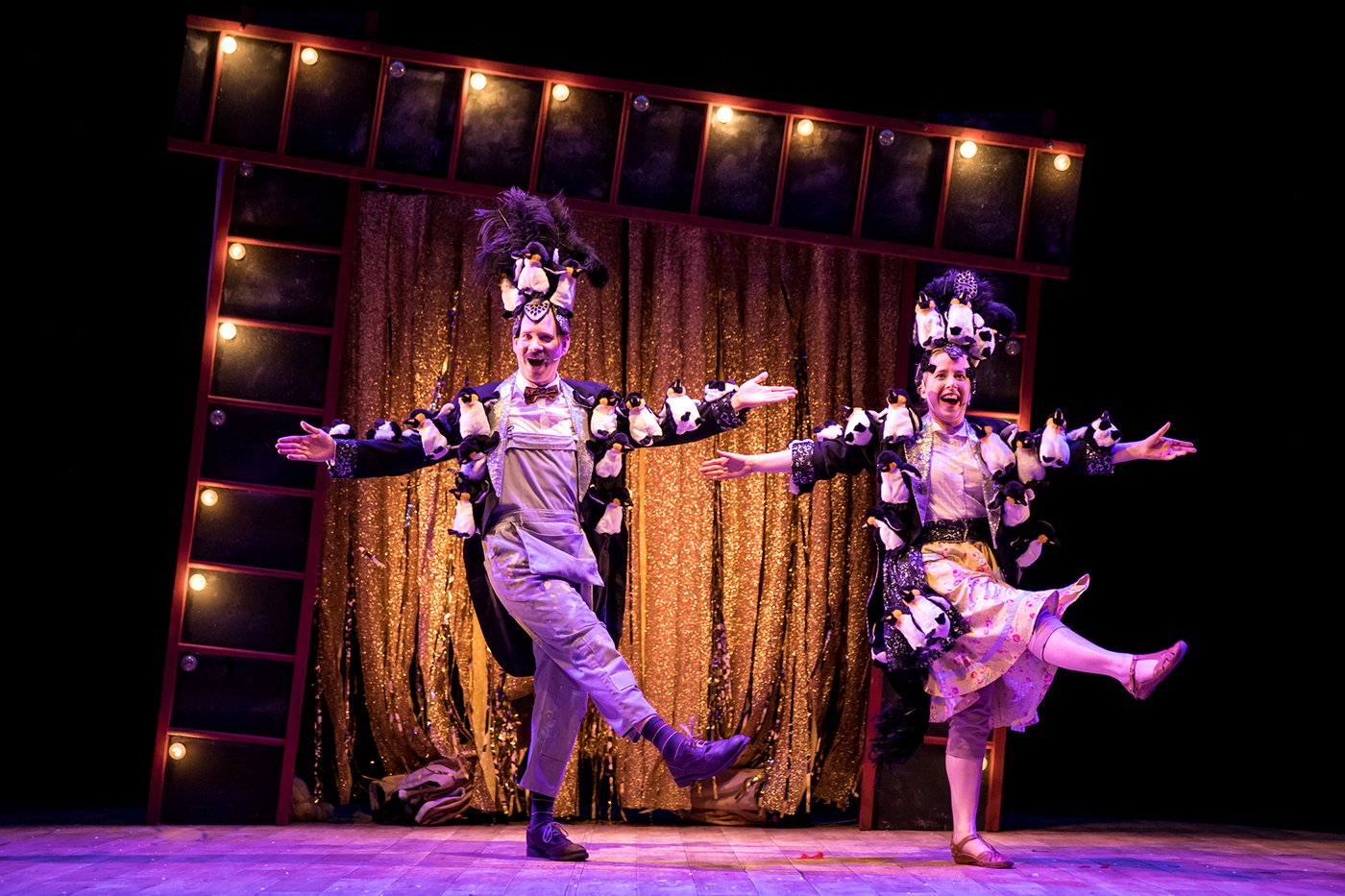two people on stage dancing with puppet penguins on their costumes