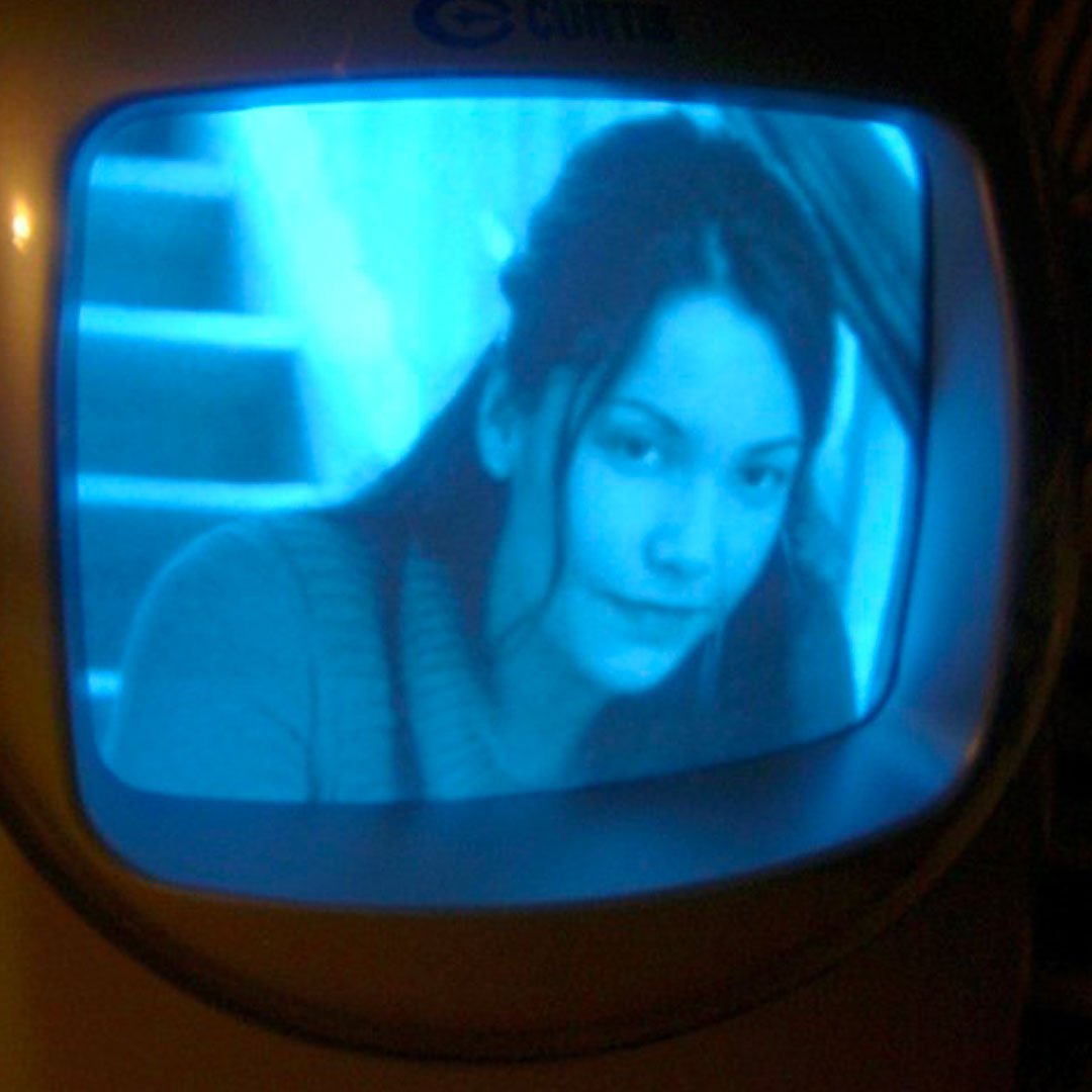 Alt text:  Promotional image showing a close-up of a person displayed on the screen of a vintage CRT television. The image is tinted in blue tones, with the television frame visible around the screen, creating a retro film and television aesthetic.