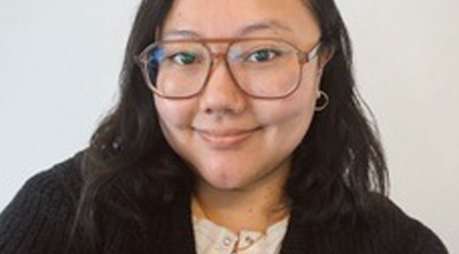 This image is a color head-and-shoulders portrait of a person positioned against a plain, light-colored background.