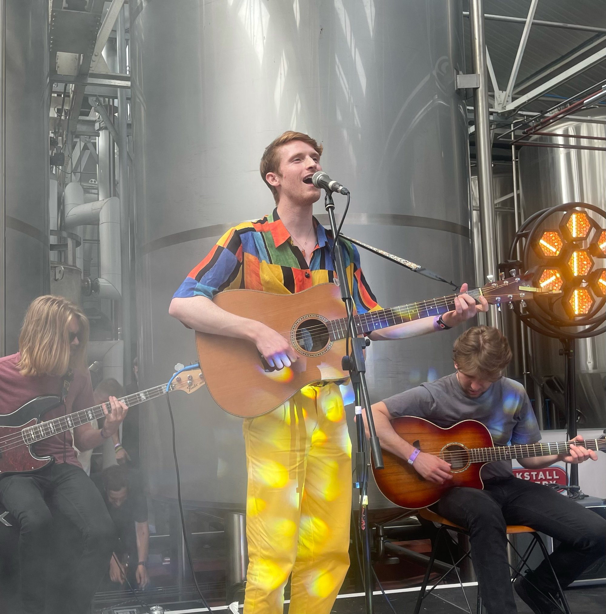 Bay Bryan standing at a mic singing while playing a guitar