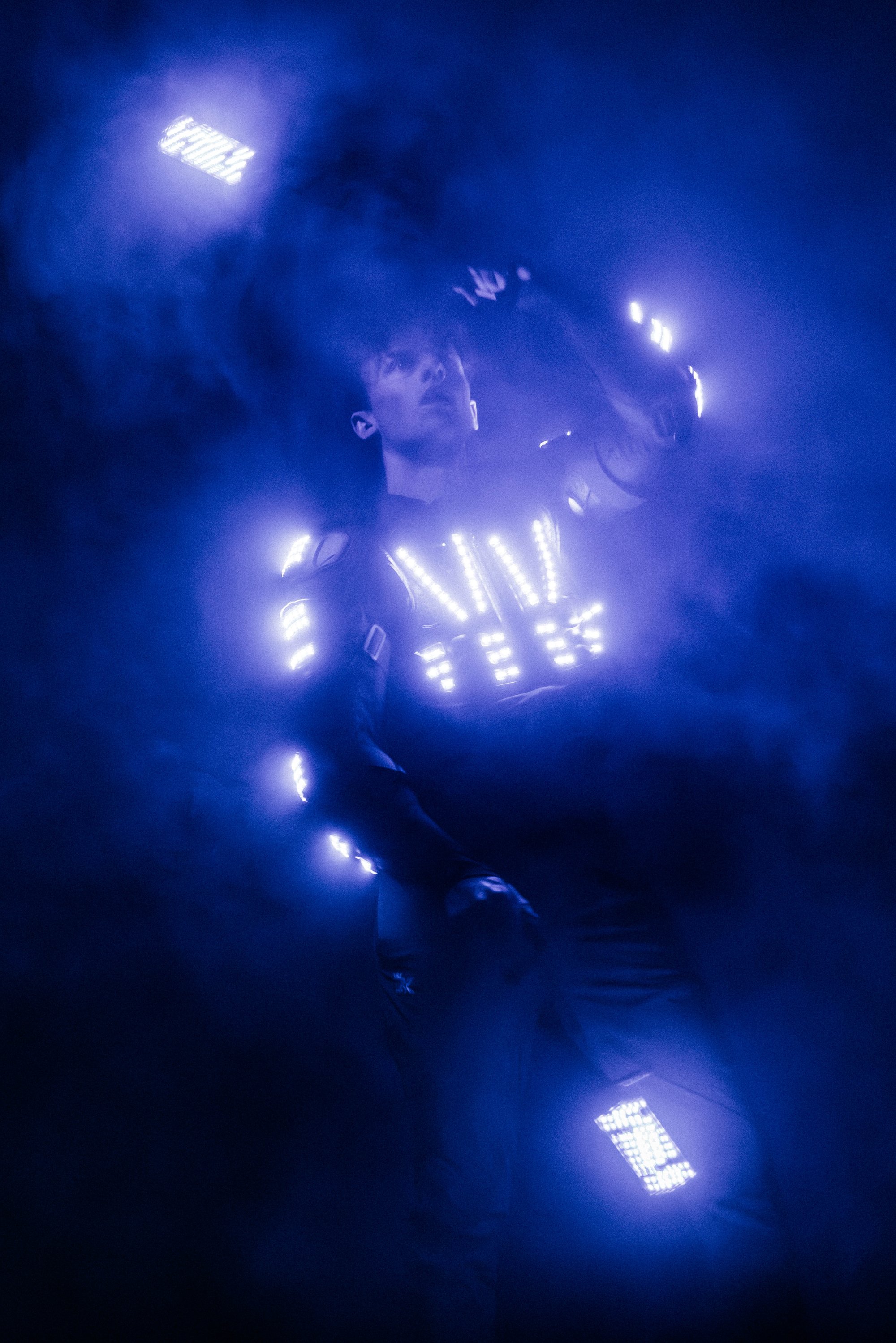 Performer in a glowing LED suit surrounded by blue haze, interacting with illuminated light panels