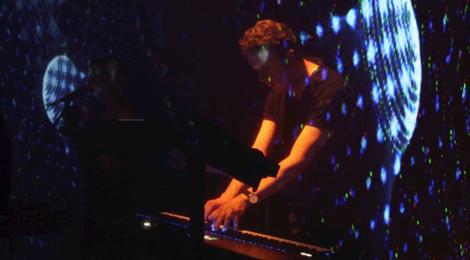 A man playing a keyboard with atmospheric blue and orange lighting