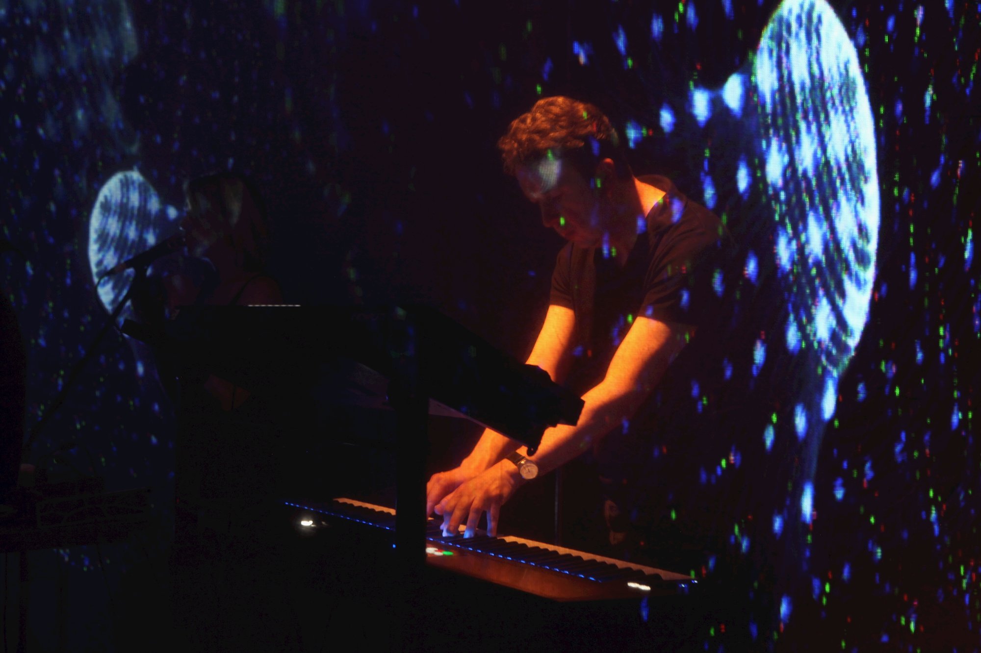 A man playing a keyboard with atmospheric blue and orange lighting