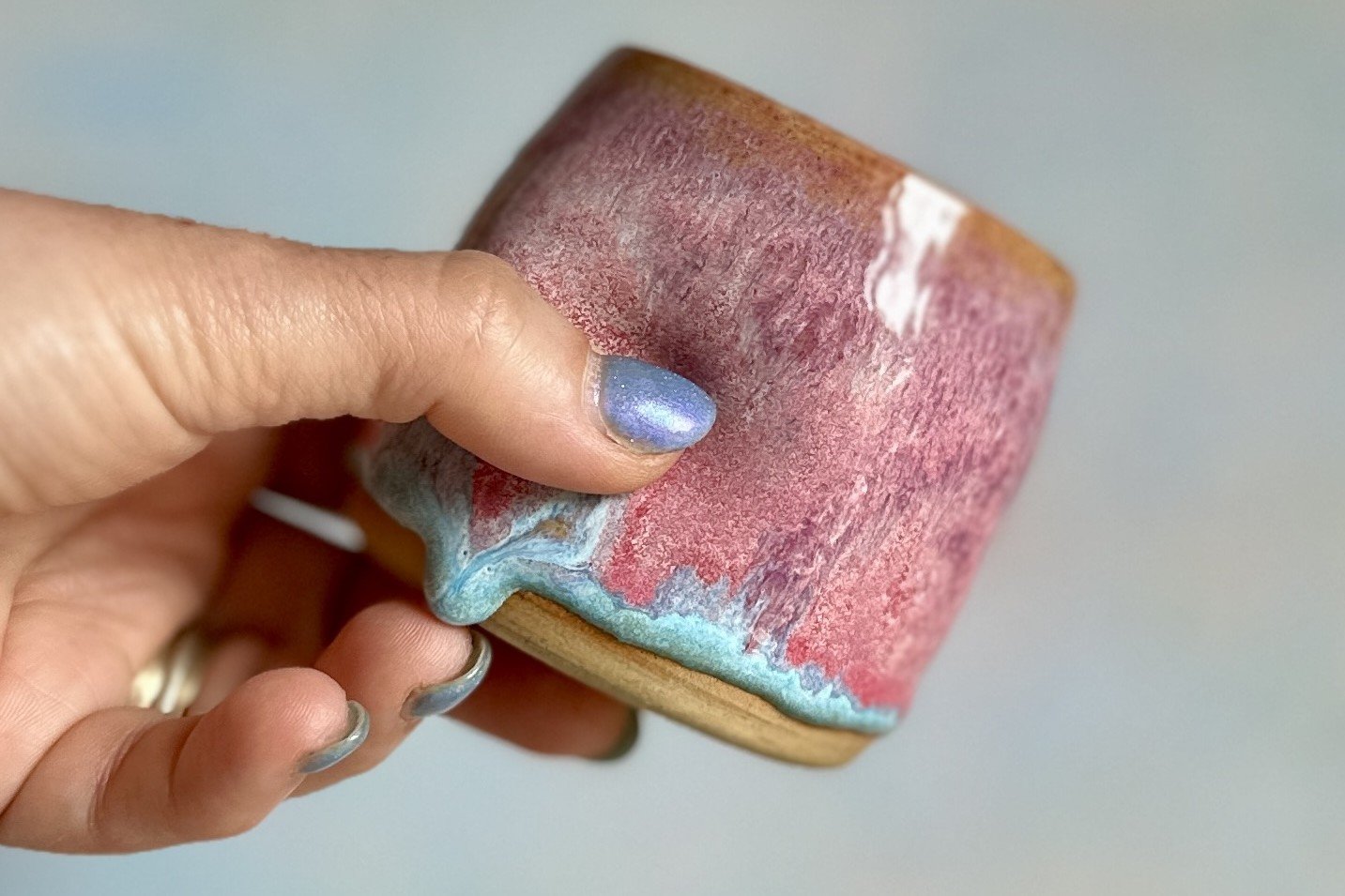 Pink and turquoise glazed pot being squeezed in someone's hand