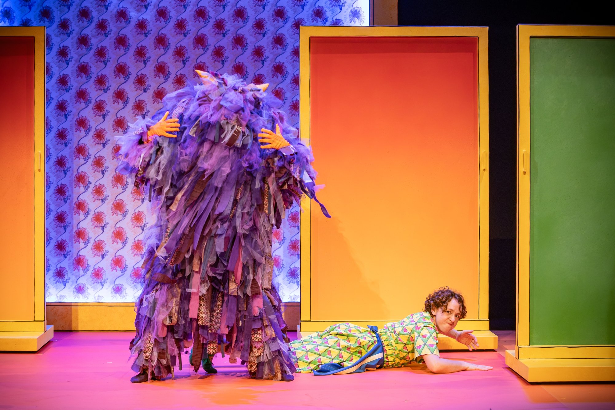 A purple fluffy monster stood on stage with someone crawling on the floor next to them