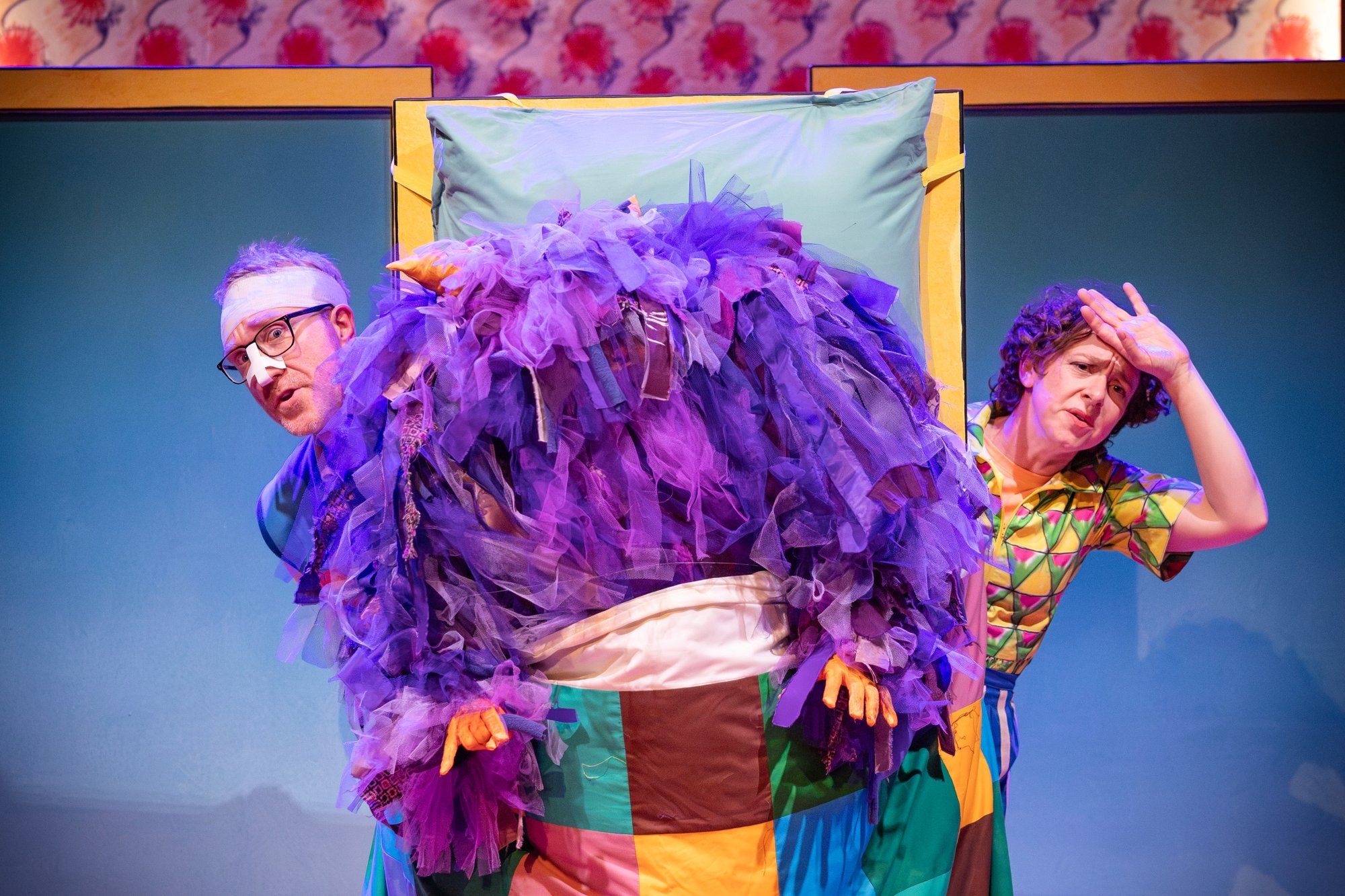Two people peeping out behind a purple fluffy monster
