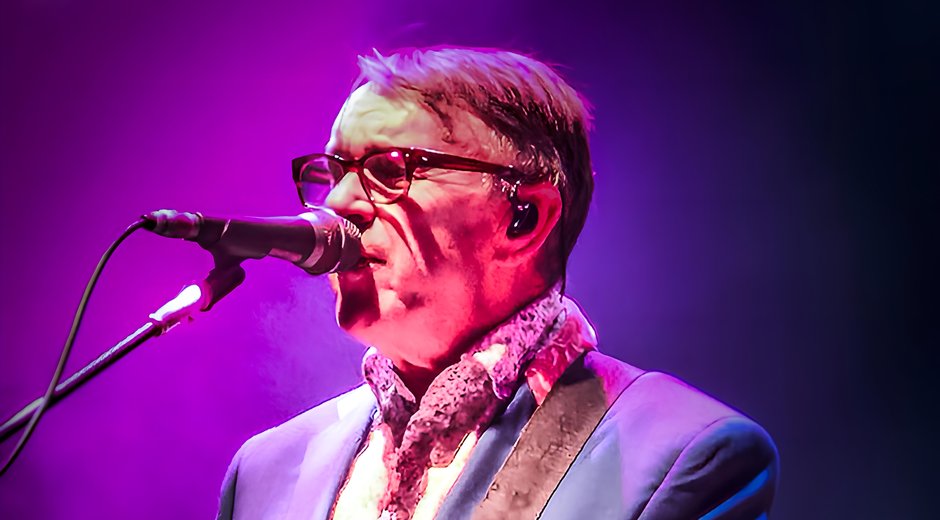Chris Difford playing a guitar and singing at a microphone