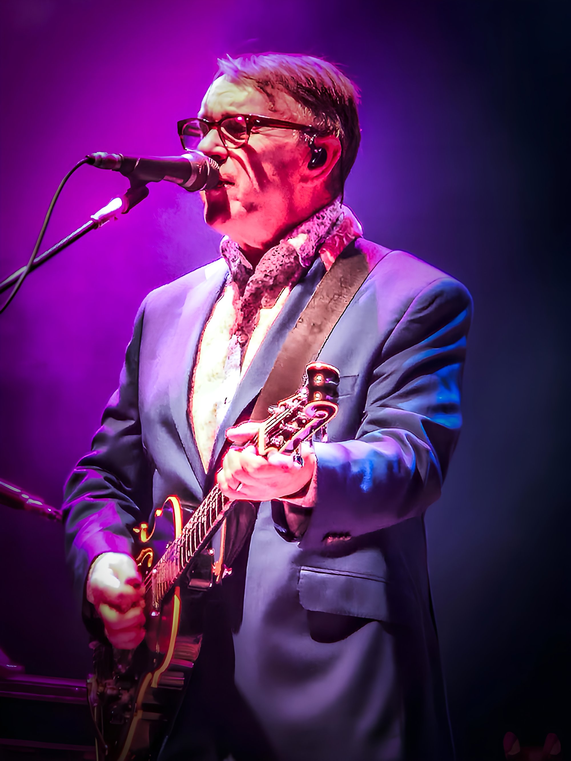 Chris Difford playing a guitar and singing at a microphone