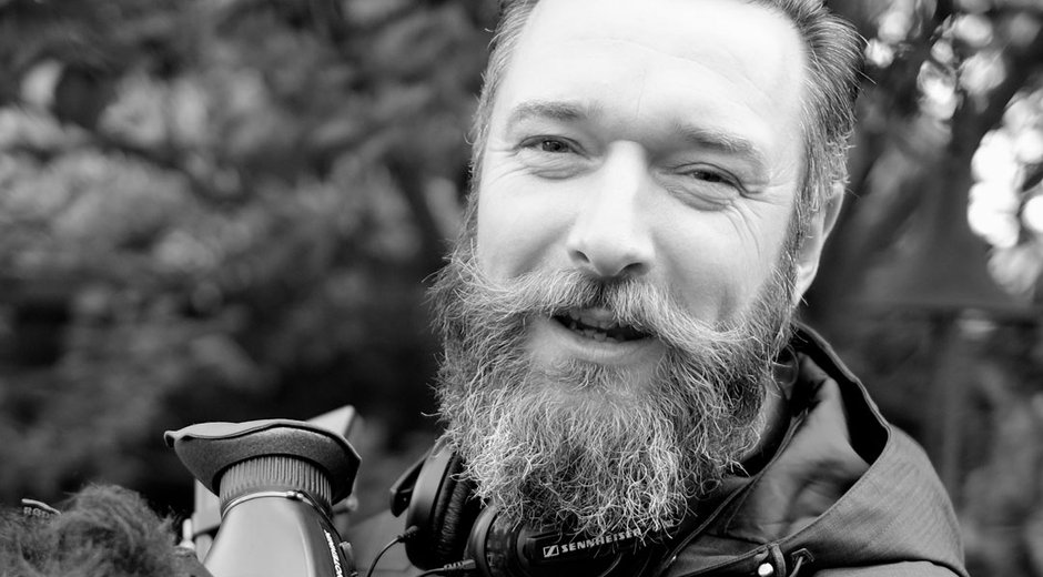 This is a black-and-white close-up portrait of a person outdoors, photographed from the chest up.