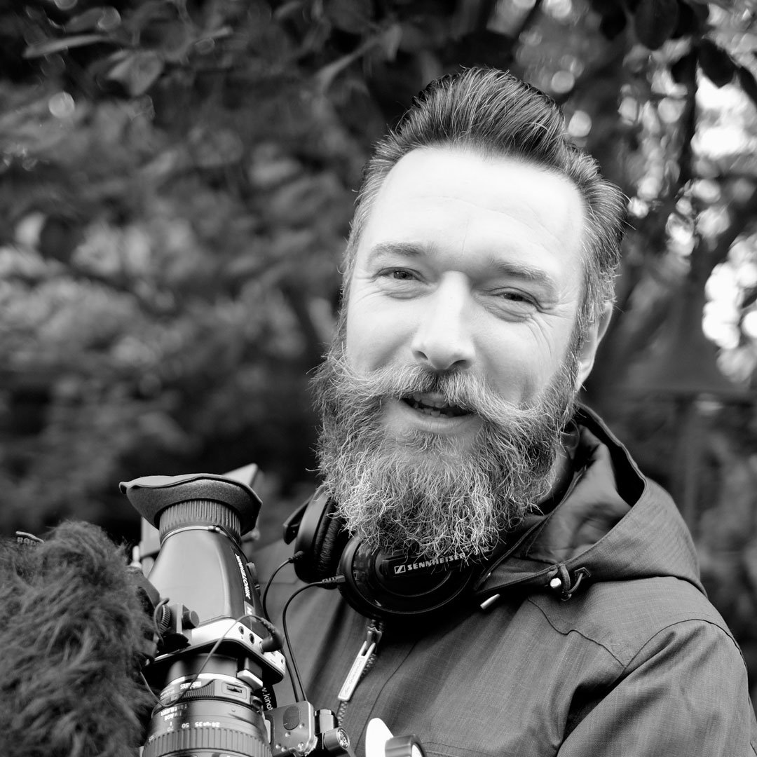 This is a black-and-white close-up portrait of a person outdoors, photographed from the chest up.