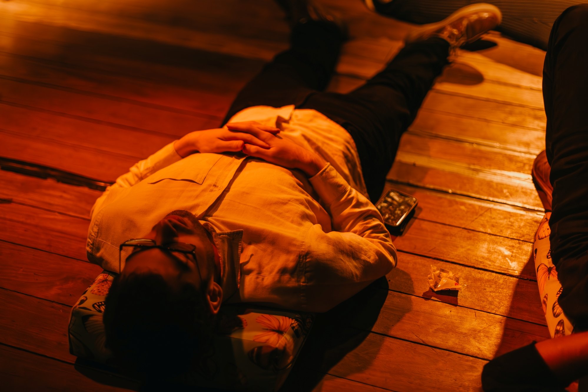 An audience member lies in a performance space bathed in orange light, during an immersive sound experience.